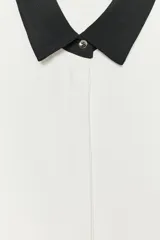 Camisa blanca de manga larga con cuello y puños negros. Cierre frontal con botones.