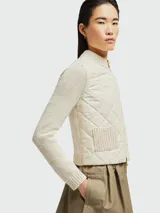 Sudadera color crema con mangas largas de punto, cuerpo acolchado con patrón de rombos, cierre frontal con cremallera dorada y bolsillos de parche.