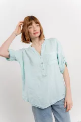 Camisa celeste de lino con cuello mao, escote en V abotonado, bolsillo en el pecho y mangas 3/4 con trabilla.