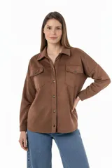 Camisa marrón de gamuza sintética, corte amplio y largo irregular. Tiene cuello clásico, cierre frontal con botones a presión, dos bolsillos con solapa abotonada en el pecho y mangas largas con puños abotonados.