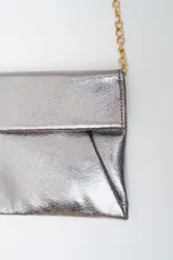 Cartera tipo sobre o clutch de color plateado/bronce metálico, con solapa frontal y correa de cadena fina dorada.