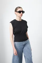 Top sin mangas negro de tejido acanalado, con hombros definidos y un recorte elástico bajo el busto que ajusta la silueta.