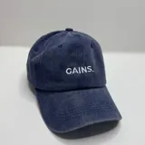 Gorro color beige con visera y bordado frontal con la palabra "GAINS" en color blanco.
