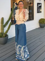 Pantalón palazzo de jeans azul con bordado floral blanco en el ruedo y cintura alta con cinturón ancho color beige con tachas.