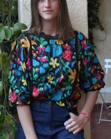 Camisa negra con estampado floral multicolor, cuello redondo con detalle de encaje negro, mangas 3/4 abullonadas con puños elásticos y corte holgado.