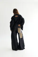 Pantalón de jean negro de corte acampanado, con parches de pana color visón y cordones en la cintura.