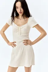 Vestido corto color crema, de punto acanalado, con escote corazón ribeteado en encaje y cordón para ajustar en el centro del busto. Modelo de manga corta con cuerpo entallado y falda con vuelo.