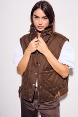 Chaleco reversible de algodón con acabado lavado y diseño acolchado con pespuntes ondulados. Presenta cuello alto con cordón ajustable, cierre frontal de cremallera y botones a presión, bolsillos delanteros tipo parche y cordón de ajuste en el bajo.