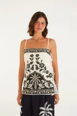Top sin mangas color blanco con estampado de flores y hojas en negro. Tiene tirantes finos ajustables y lazo en la parte delantera.