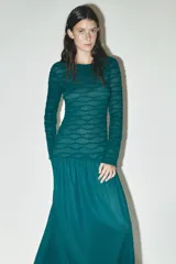 Vestido midi color verde esmeralda con textura plisada en la parte superior y falda lisa. Tiene cuello redondo y mangas largas.