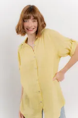 Camisa amarilla de lino con corte recto y calce suelto. Tiene cuello camisero, botones en el frente y mangas cortas con presilla y botón.