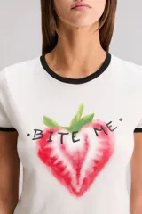 Remera blanca de calce slim, escote redondo y manga corta, con ribete negro en cuello y mangas. Estampa frontal de una frutilla roja con la frase "Bite Me".