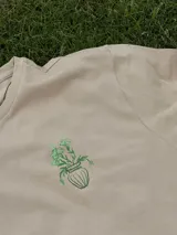 Remera color arena de manga corta con estampa en la espalda de un jarrón con flores.