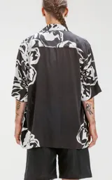 Camisa de manga corta negra con estampado de flores blancas, calce oversize y canesú en la espalda.