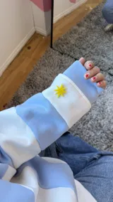 Buzo deportivo celeste y blanco a rayas horizontales, con cuello redondo amarillo y puños y ruedo en celeste.