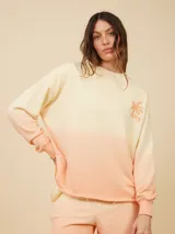 Sweater color crema con degradé a naranja, con cuello redondo y logo estampado de palmera en el pecho.