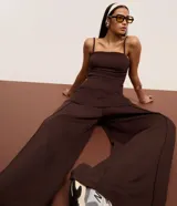 Pantalón de mujer color marrón oscuro, de tiro alto con cintura elástica fruncida y corte ancho recto. Presenta vincos delanteros marcados.