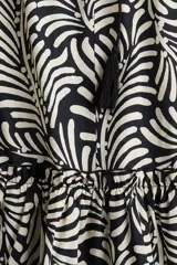 Vestido corto de algodón con estampado abstracto en blanco y negro. Tiene cuello con volados y lazo con borlas, mangas largas abullonadas con puños elásticos y falda escalonada con volados.