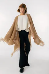 Ruana de punto color beige con cuello alto y flecos.