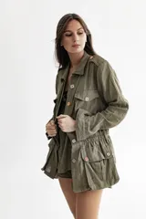 Chaqueta verde militar de lino, estilo cazadora, con cuello clásico, cierre frontal con botones decorativos, bolsillos con solapa en pecho y cadera, cintura elastizada y manga larga.