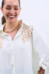 Camisa color crudo con bordado de lentejuelas doradas en el frente, de corte holgado y mangas largas con lazo en los puños.