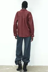 Camisa color borgoña a rayas verticales finas, de corte recto, con cuello solapa y manga larga. Tiene dos bolsillos de parche con solapa en el pecho y cierre frontal con botones.