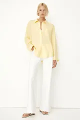 Camisa amarilla de tejido liviano de mezcla de lino y viscosa con cuello, botones adelante y canesú de doble capa con pliegue de caja en la espalda. Modelo de manga larga con bolsillo superior abierto, puños abotonados y bajo redondeado.
