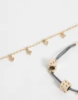Set de dos pulseras doradas, una con cadena y dijes colgantes de strass con forma de trébol, corazón, rombo y flor. La otra pulsera es de hilo de lurex gris con cadena dorada y dijes de dados dorados.