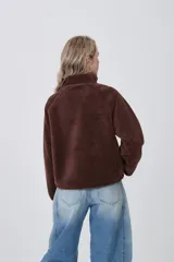 Campera de poliéster tipo sherpa en color natural, con diseño holgado, cuello alto y cierre frontal completo. Presenta un bolsillo de parche con cierre en el pecho y mangas largas con puños elásticos.