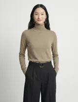 Polera de punto fino marca Nienty, color blanco, con cuello alto volcado y mangas largas con detalle de tajo en los puños.