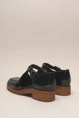 Zapato guillermina de cuero vacuno charol color negro, con suela de goma color marrón.