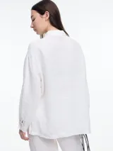 Camisa de manga larga de lino color azul con calce relajado y diseño asimétrico. El bolsillo delantero está colocado de forma invertida, un detalle lúdico que rompe con lo clásico. Lleva un bordado tipo pespunte en color contraste que recorre el frente y el bolsillo.