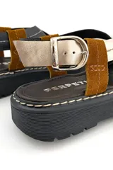 Sandalias de cuero con tiras cruzadas color marrón, negro y dorado, con hebilla de ajuste y suela de goma negra.