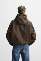 Cazadora relaxed fit confeccionada en tejido de algodón denim color marrón. Cuello con capucha ajustable y manga larga. Bolsillos frontales tipo canguro. Acabados con elástico. Efecto lavado. Cierre frontal de cremallera.