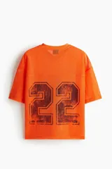 Remera de malla color naranja vibrante, estilo jersey de fútbol americano, con cuello en V y corte oversized. Presenta un estampado grande y desgastado del número "22" en color negro o marrón oscuro en el frente.