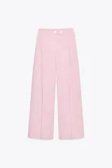 Pantalón ancho color rosa claro, de tiro alto con pinzas delanteras, bolsillos frontales y cierre frontal con cremallera y botones.