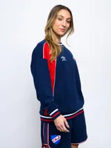 Buzo de felpa azul marino con mangas raglán rojas y detalles tricolor en puños, mangas y cuello. Incluye logo de Umbro bordado en el pecho y escudo del Club Nacional de Football.