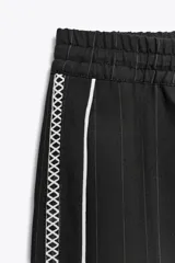Pantalón de tiro alto negro a rayas verticales blancas, con cintura elástica ajustable con cordones, bolsillos delanteros y banda lateral blanca.