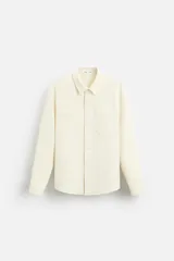 Sobrecamisa color crema de tejido con elasticidad, cuello solapa, manga larga con puño abotonado, bolsillos de parche en el pecho y cierre frontal con botones a presión.
