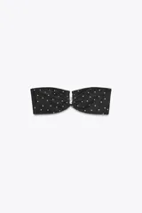 Top de bikini bandeau negro con estampado de lunares blancos, copas extraíbles, hombros descubiertos y pieza metálica forrada en el pecho.