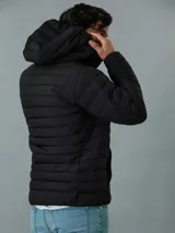 Campera acolchada negra con capucha, cierre frontal con cremallera y bolsillos laterales con cremallera. Logo de Calvin Klein en el pecho.