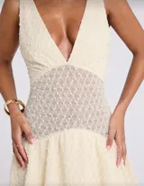 Minivestido color crema con textura de lunares, escote en V, corte en la cintura con detalle de encaje y falda con volados. Sin mangas.