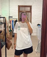 Remera blanca de corte holgado con cuello redondo y manga corta. Presenta un pequeño estampado frontal con texto en rosado y un limón cortado.