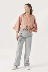 Camisa corta color rosa pálido, con cuello, escote en V y cierre frontal anudado. Presenta mangas anchas y caídas.