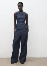 Top crop sin mangas, color azul oscuro, con cuello redondo y tirantes anchos. Presenta un efecto denim y cierre de botón en la parte trasera del cuello.