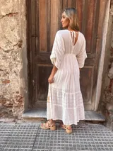 Vestido largo blanco con escote en V profundo y mangas cortas con volantes. Presenta detalles bordados o estampados en hilo dorado en el escote y en los volantes de la falda, con un ajuste fruncido en la cintura.