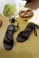 Sandalias bajas de cuero color marrón, con tiras finas para atar alrededor del tobillo.