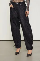 Pantalón negro con estampado de piel de serpiente, de tiro bajo y corte holgado, con puños ajustables con lazos.