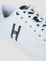 Zapatillas urbanas de corte bajo, color blanco, con cordones y suela de goma. Presentan un gran logo 'H' en color azul marino en el lateral y detalles en azul marino en el talón y la lengüeta.