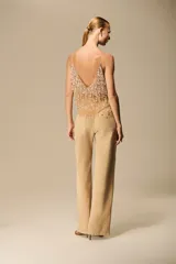 Pantalón de sarja color beige, tiro medio, de corte recto y pierna ancha, con apliques brillantes tipo joya en la parte delantera.